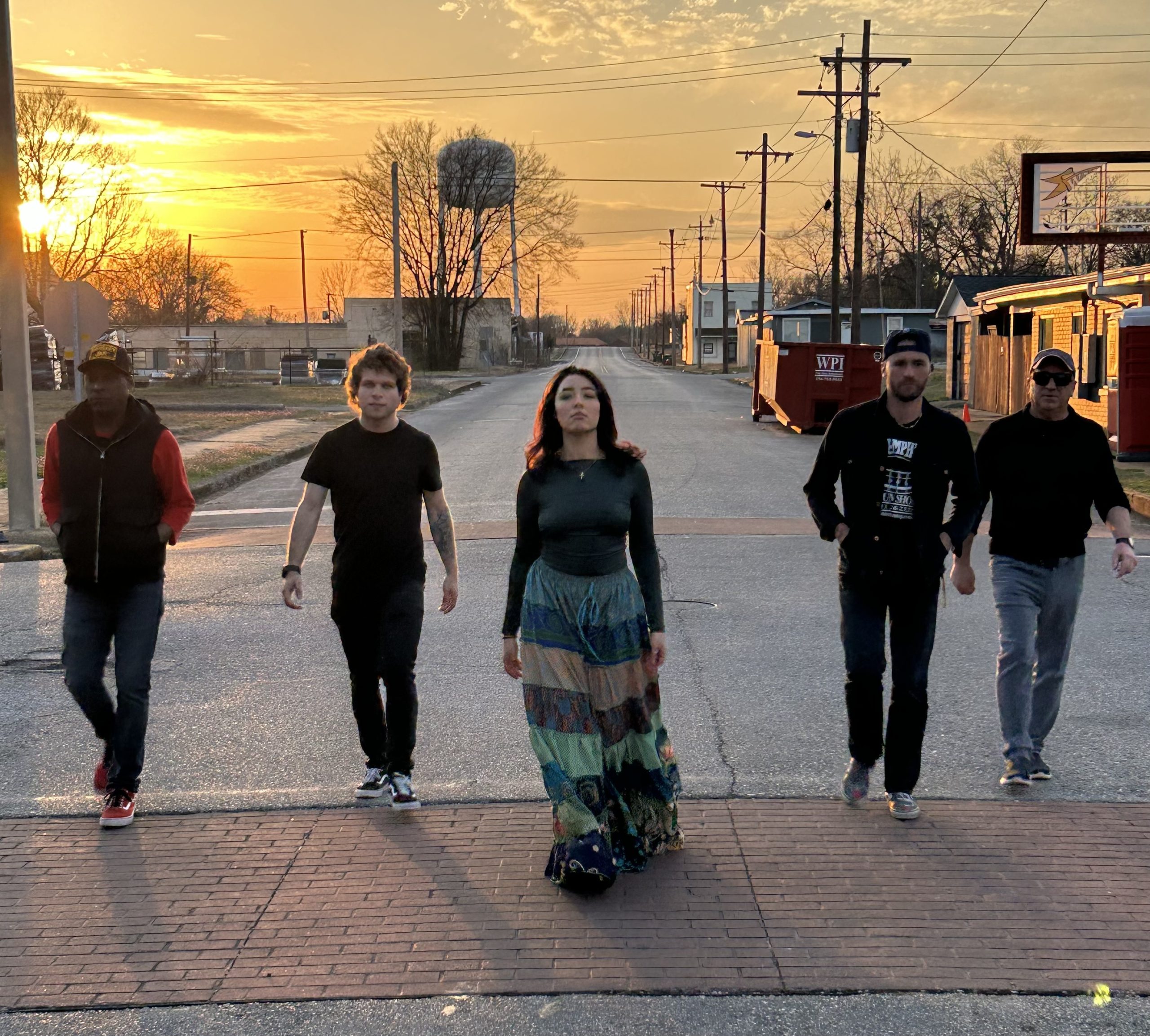 The members of the Saycouth band walk towards the camera during a sunset, on a street in a small town.